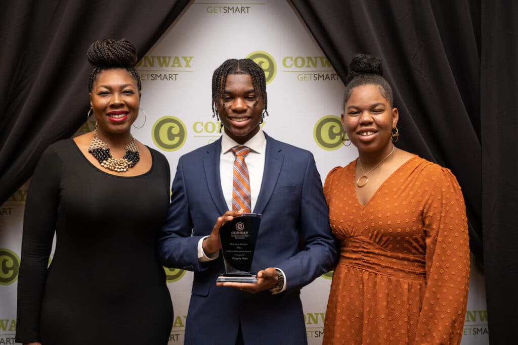 A young man in a suit holding an award with his family.