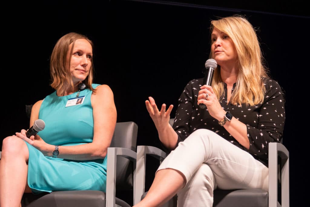 Two women sit on a stage speaking at an event.