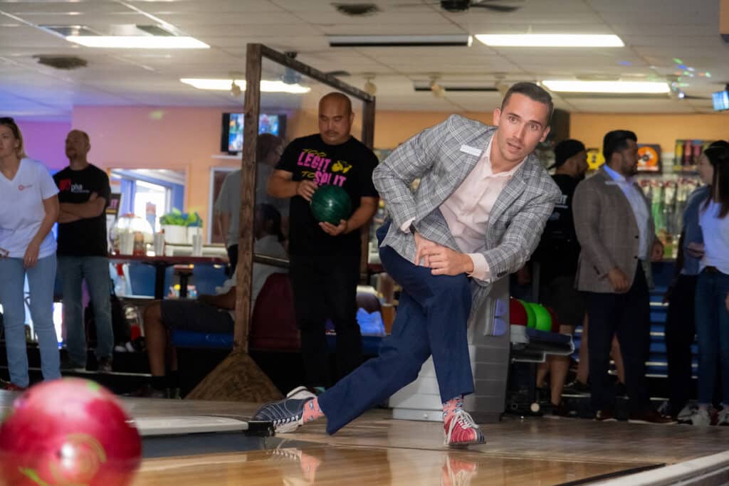A man in business clothes bowling at a networking event.